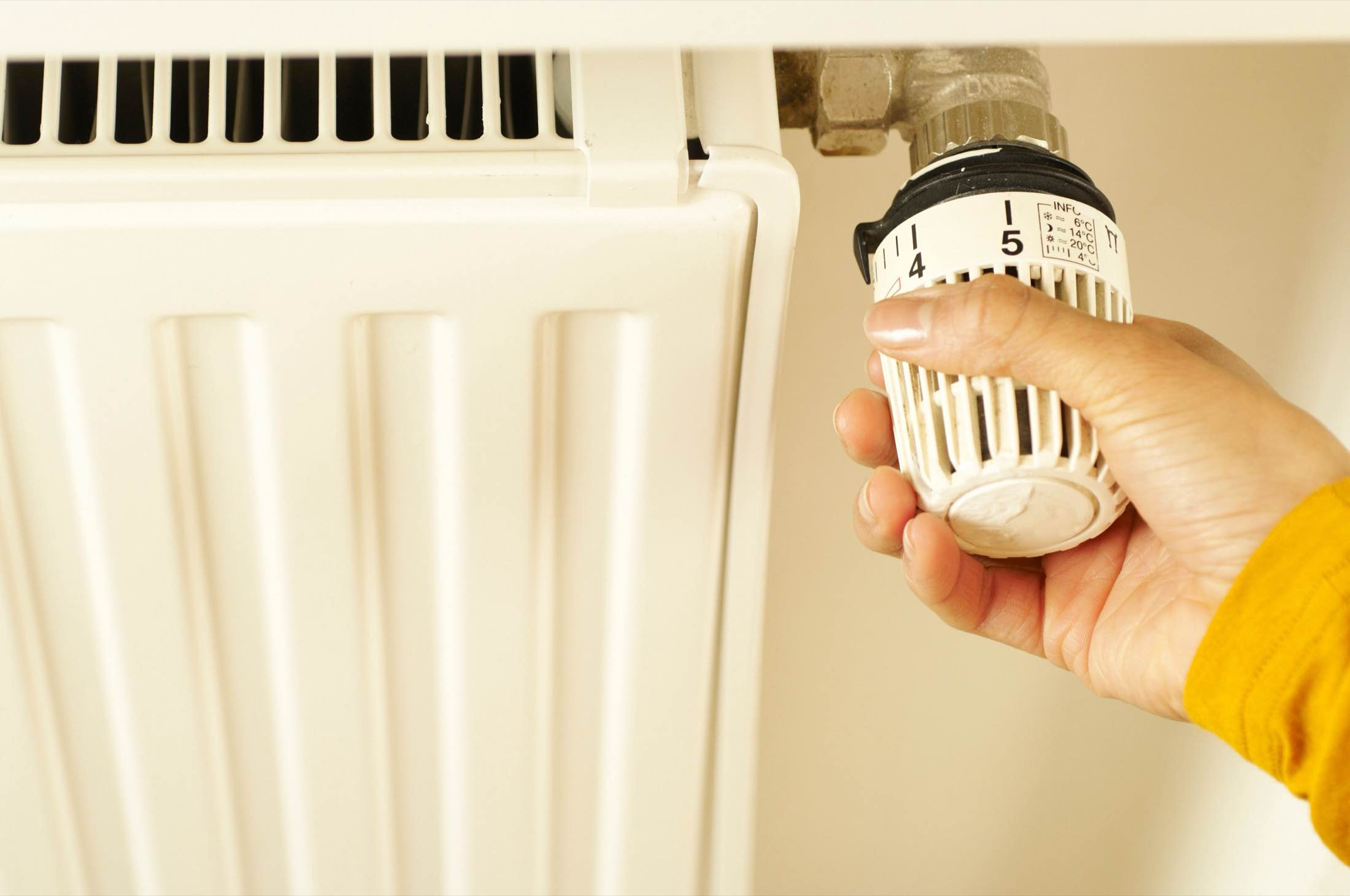 A hand turning the dial of a manual radiator valve