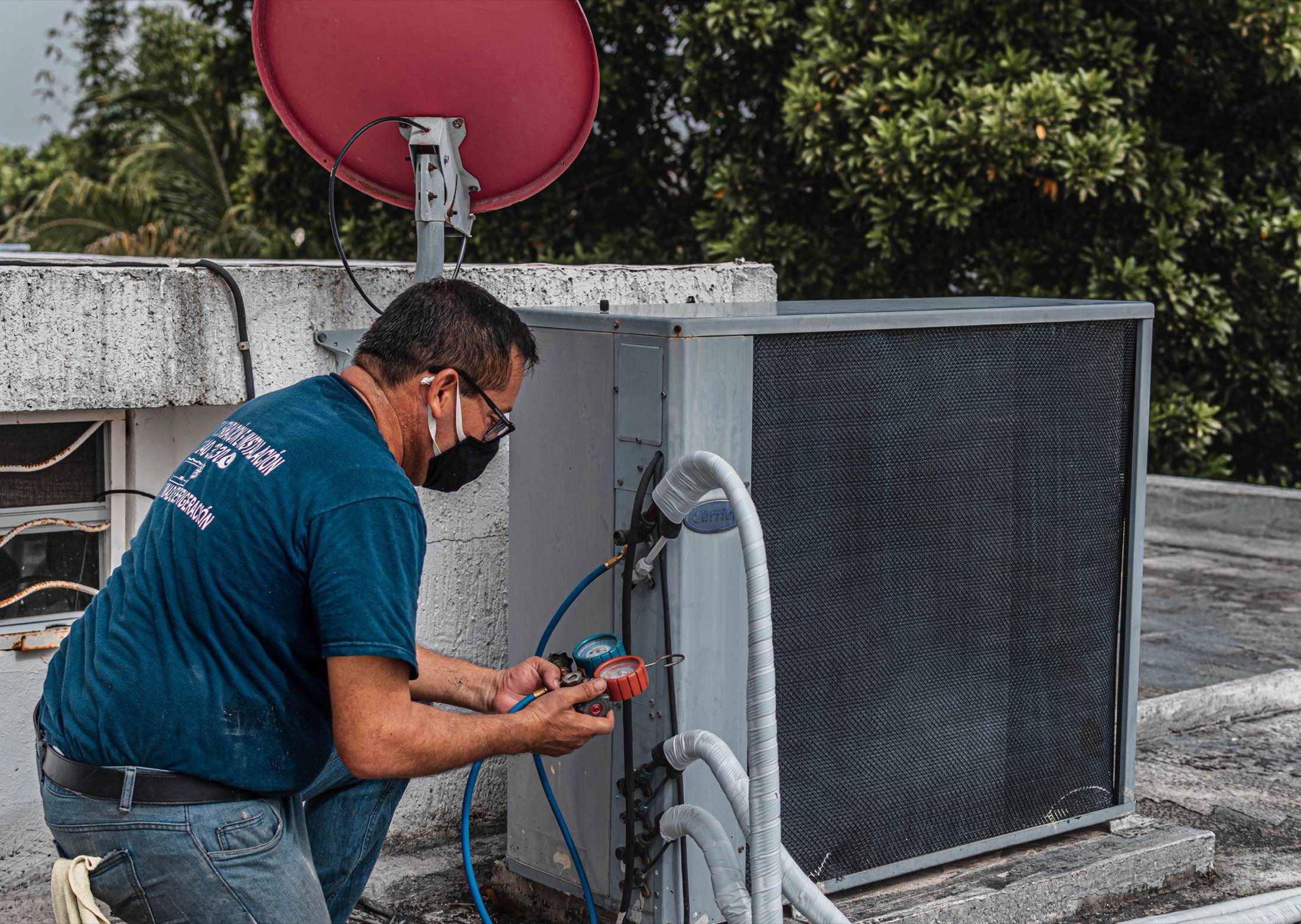 A technician servicing an outdoor condensing unit with gauges attached